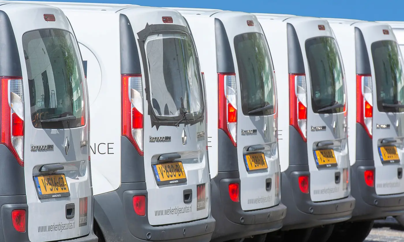 A row of white commercial vans parked side by side at a depot