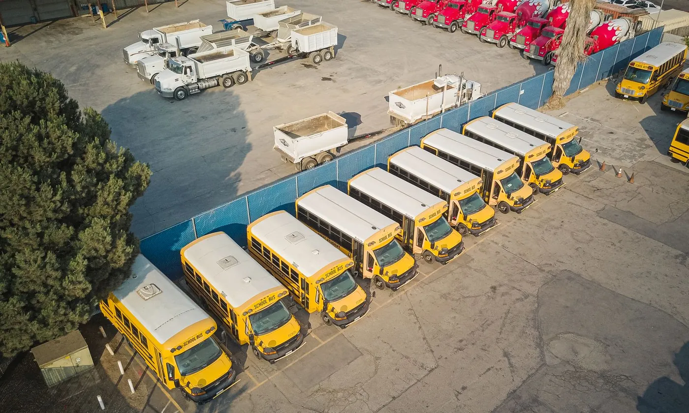 Aerial view of a yard holding several vehicle classes: school buses, tipper trucks and concrete mixers